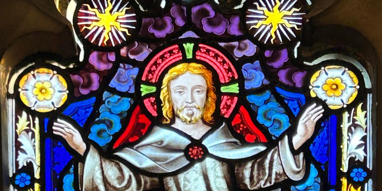 Stained glass window depicting Jesus with raised hands.