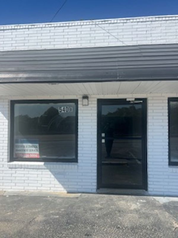 Closed storefront with white brick exterior and black door.