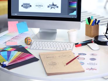 Creative workspace with logo designs, color swatches, and drawing tools on a white desk.
