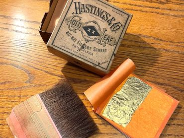 Vintage Hastings & Co. gold leaf box with a brush and gold leaf sheets.