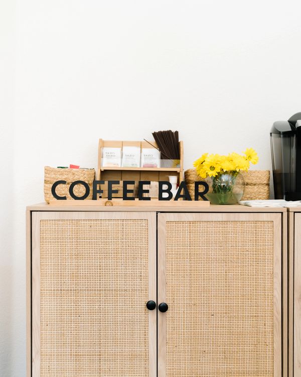 Minimalist coffee bar setup with a wooden cabinet and yellow flowers.