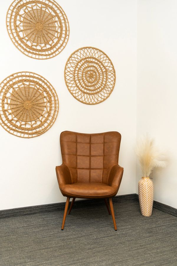 Brown leather chair with woven wall decorations and a vase with pampas grass.