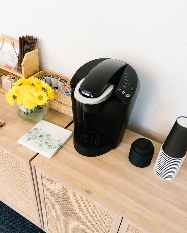 Keurig coffee maker setup with yellow flowers and disposable cups on wooden cabinet.