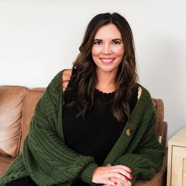 Smiling woman in a cozy green cardigan sitting on a couch indoors.