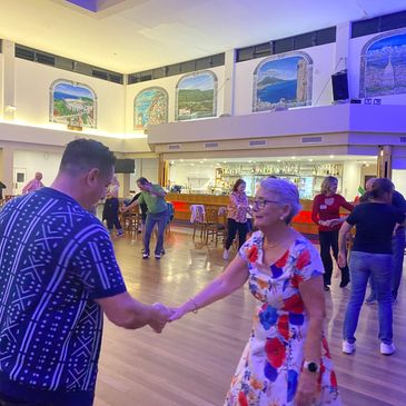 People rock’n’roll dancing in a spacious hall with vibrant wall murals and bar area.