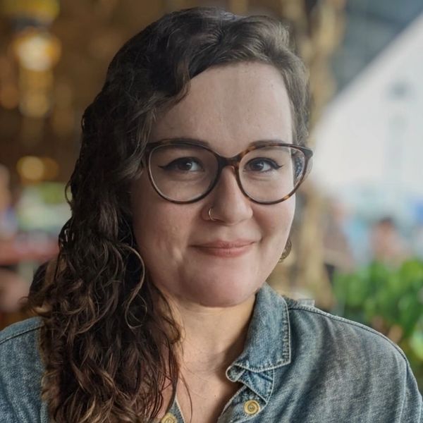 Smiling woman with glasses and curly hair in a denim jacket.