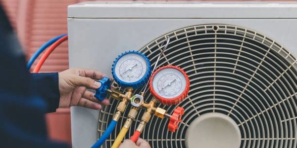 Technician adjusting HVAC gauges on an air conditioning unit outdoors.