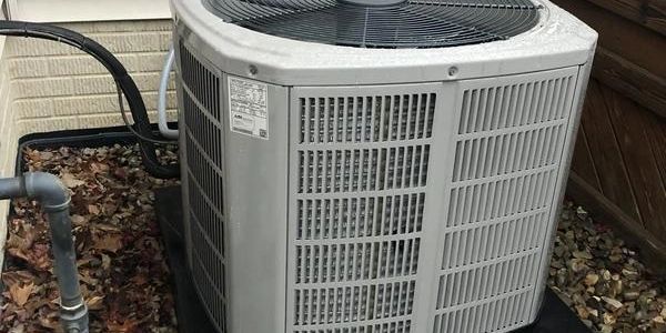 Outdoor air conditioning unit installed on a bed of rocks beside a house.