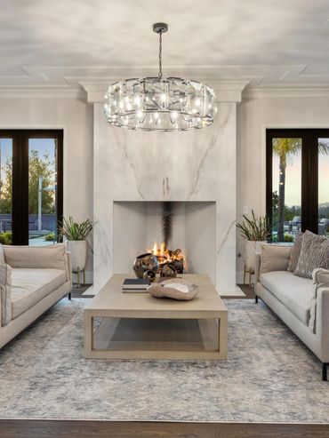 Elegant living room with twin sofas, a marble fireplace, and a modern chandelier.