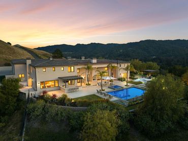 Luxurious modern mansion with a pool at sunset in a scenic mountainous area.