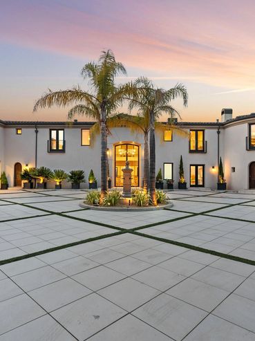 Elegant courtyard with palm trees and modern mansion at sunset.
