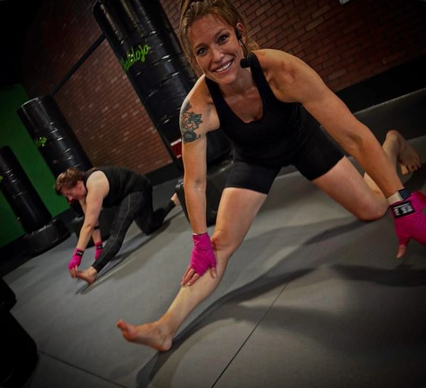 Two women stretching in a gym wearing workout gloves and athletic wear.