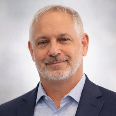 Smiling middle-aged man with gray hair and beard in business attire.