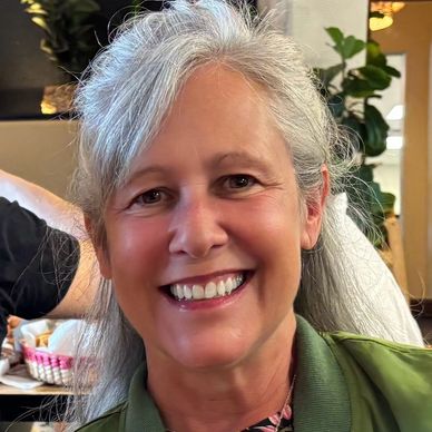 Smiling woman with gray hair and green jacket indoors.