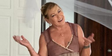 Smiling woman in a casual dress gestures indoors.