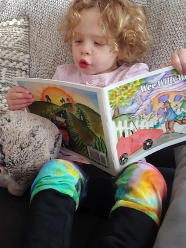 Child reading a colorful book with a stuffed animal.