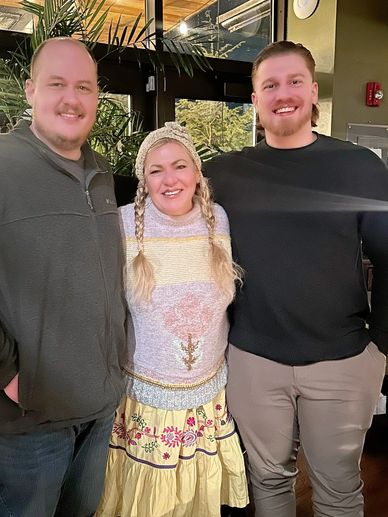 Three friends smiling indoors with casual winter clothes.
