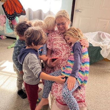 Older woman surrounded by children, all looking at a phone.