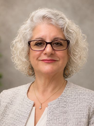 Confident woman with curly gray hair and glasses.