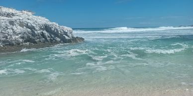Tranquil beach with clear turquoise water and rocky cliffs under a bright blue sky.
