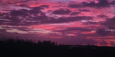 A vibrant purple and pink sunset with scattered clouds over a dark landscape.