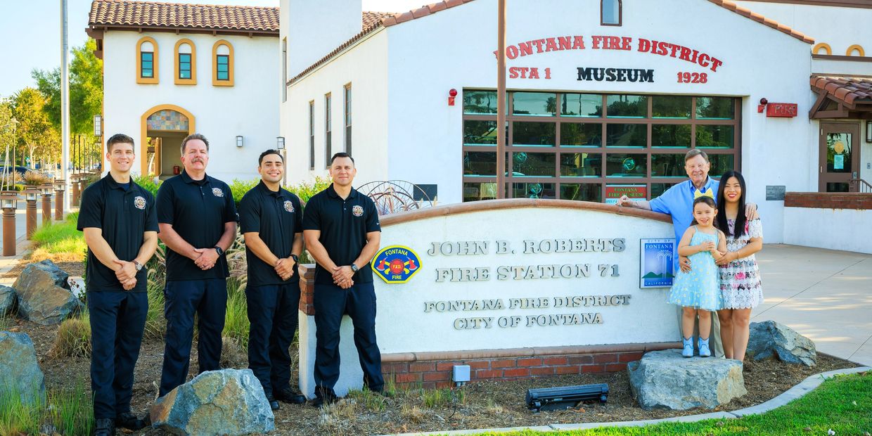A group of firefighters and family stand outside a fire station museum.