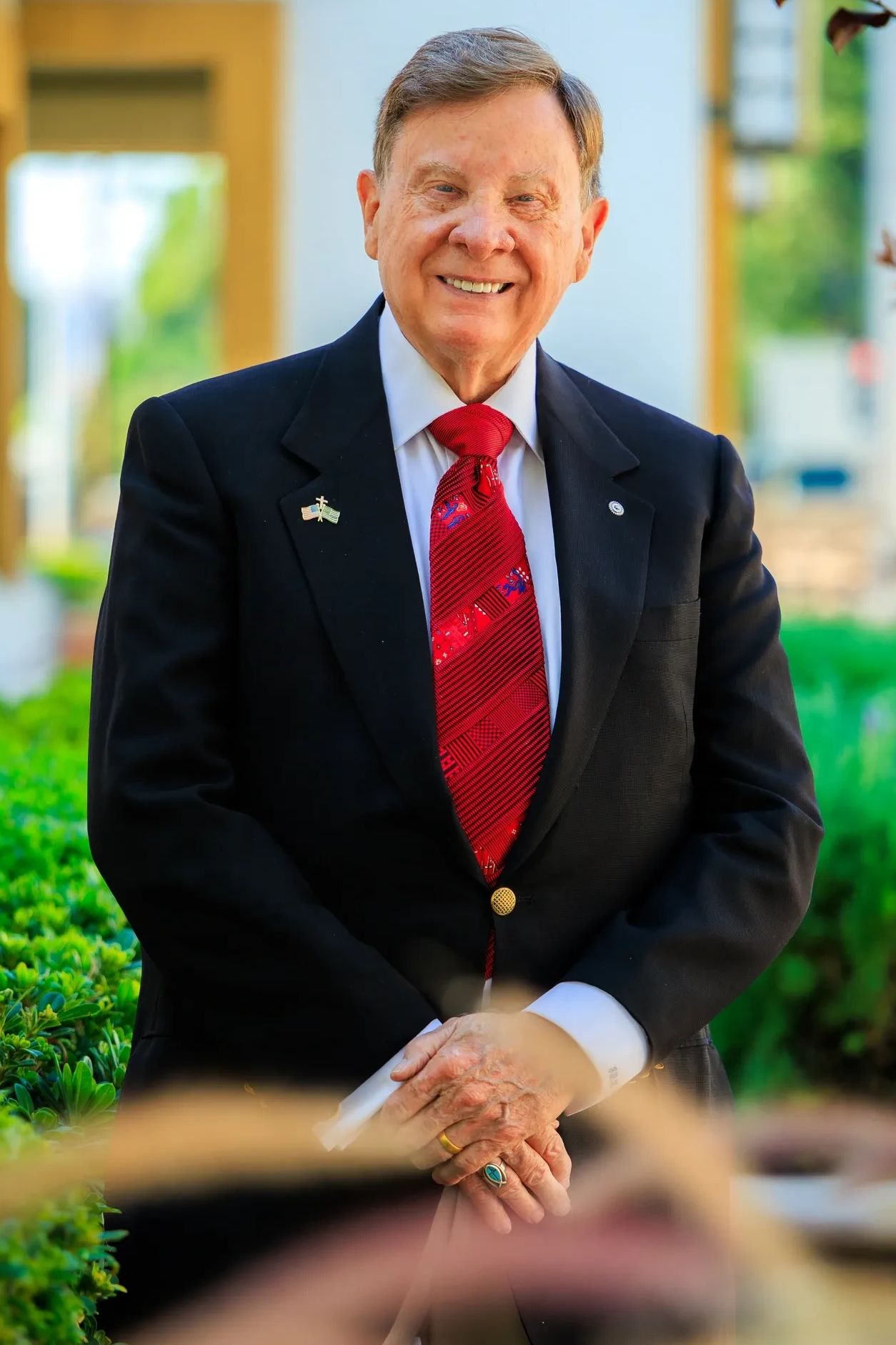 Smiling elderly man in suit with red tie outdoors.