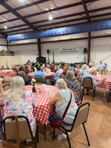 Seniors gathered at a community event with red-checkered tablecloths and a welcoming banner.