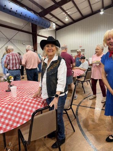 Woman in cowboy hat at a community gathering with red checkered tablecloths.