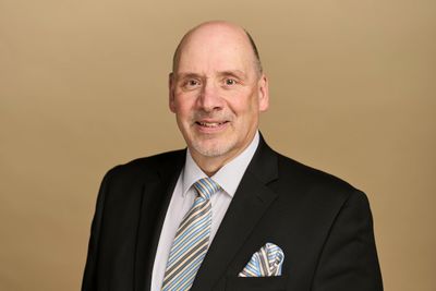 Professional portrait of a middle-aged man in a suit and tie against a neutral background.