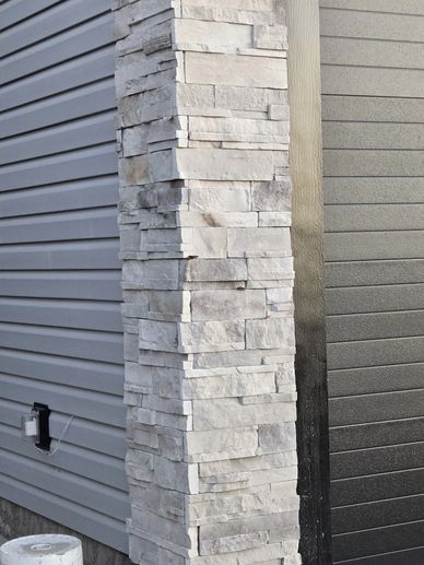 Close-up of a stone pillar next to house siding.