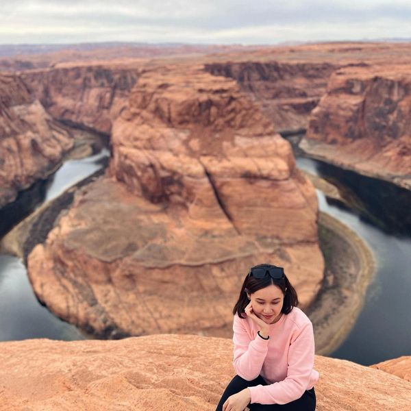 Woman in pink sweater sitting near Horseshoe Bend with scenic canyon view.
