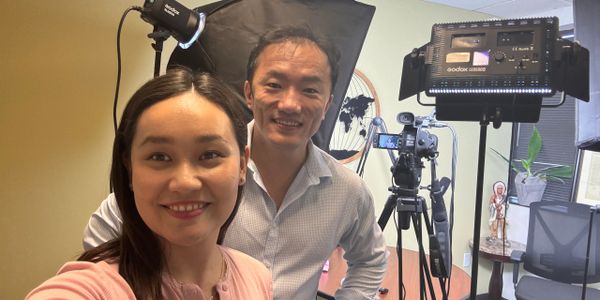 Two people smiling in a photography studio with professional lighting and camera setup.
