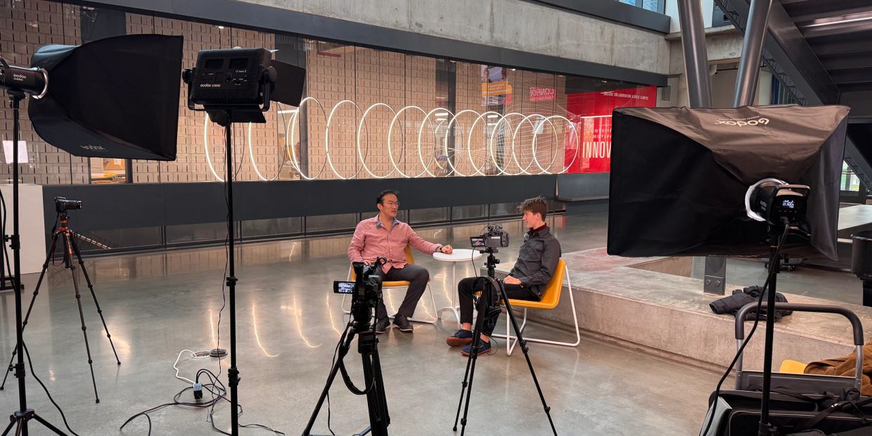 Two men seated for an interview with professional lighting and camera setup.