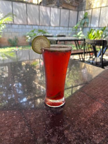 A tall glass of red drink garnished with a lime slice on a reflective table.