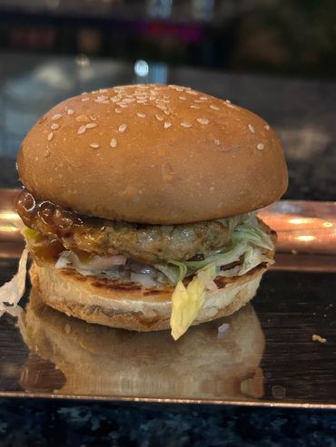 A close-up of a chicken burger with lettuce and sauce on a sesame bun.