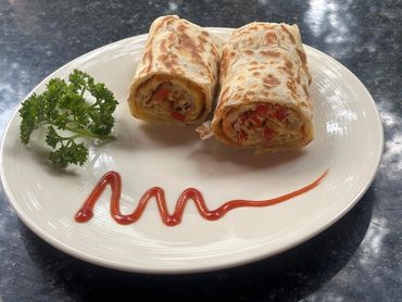 Two grilled wraps with vegetables, ketchup, and parsley on a white plate.