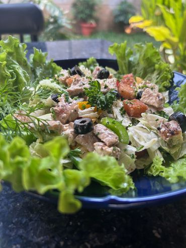 Fresh chicken salad with lettuce, olives, and herbs on a blue plate.