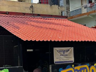 A small eatery with colorful wall art, a black Royal Enfield motorcycle, and a scooter parked outside.