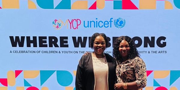 Two women pose in front of a UNICEF event backdrop titled 'Where We Belong'.