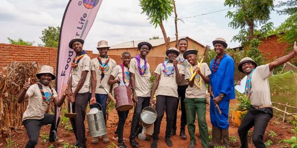 Group of scouts posing outdoors with watering cans and tools, smiling happily.