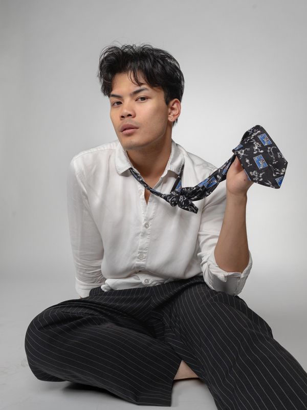 Young man sitting on the floor holding a black tie.
