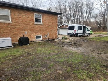 Backyard with muddy grass, a white van, and brick house wall.