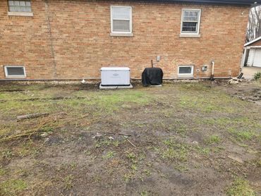 Backyard with patchy grass and two covered appliances near a brick house wall.