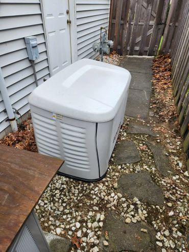 A white outdoor generator beside a house on a stone and concrete path.