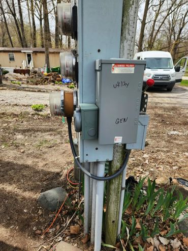 Outdoor electrical panel with utility and generator switches beside a rural home.