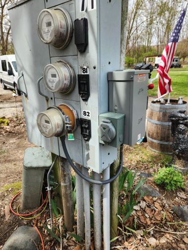 Outdoor electrical meter panel with three meters and an American flag in the background.