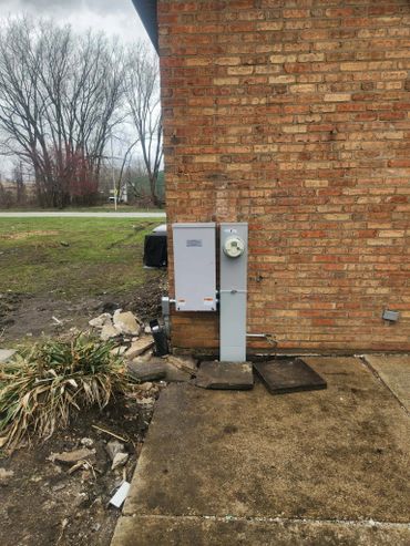Electrical meter and box installed on a brick wall outside a building.