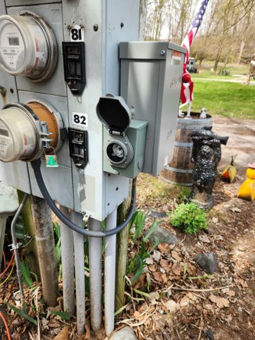 Electrical meters and outlets mounted outdoors with garden and flag in background.