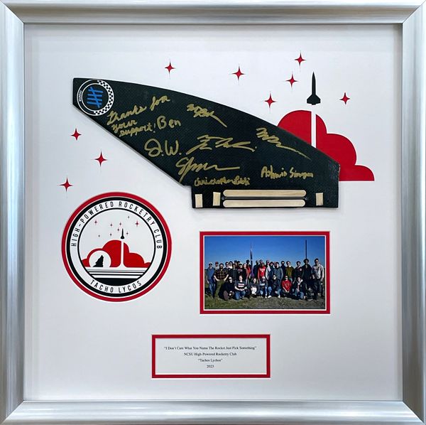 Shadowbox containing a fin from a college rocketry club, featuring the club logo & the team photo